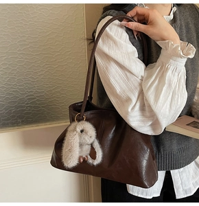 Détail d'un sac cabas marron foncé en cuir avec un pendentif lapin en peluche grise