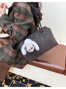 Détail d'un sac cabas gris foncé mat avec breloque peluche sur un manteau rétro