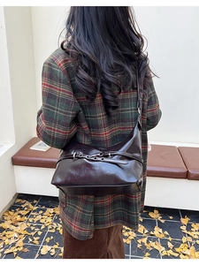 Détail du sac sous le bras en cuir marron foncé avec boucle argentée sur manteau écossais