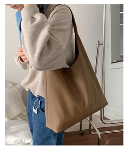 Side view of a large brown pebble leather tote bag worn by a model in a minimalist setting