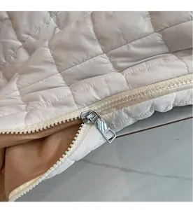 Detail of smooth silver metal zipper on white quilted puffy bag with brown lining