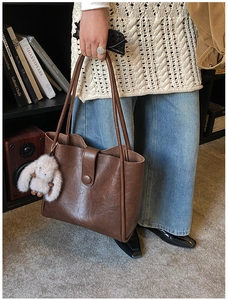 Detail of dark brown leather tote bag with plush rabbit charm and long shoulder straps