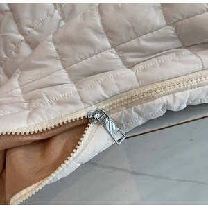 Close-up of silver metal zipper on white quilted puffer bag with khaki fabric lining