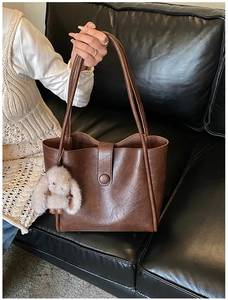Close-up of brown faux leather tote bag with long straps and a plush rabbit charm