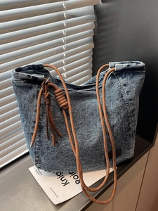Large denim tote bag with rope handles and tassel detail shown in natural light