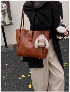 Close-up of a brown PU tote bag with a plush rabbit charm in a street style setting