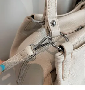 Detailed close-up of a silver metal hook and reinforced stitching on a beige leather bag