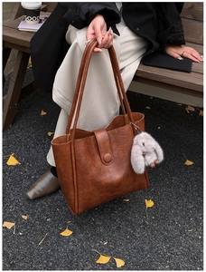 Brown vintage leather tote bag with rabbit charm shown in a cozy autumn street setting