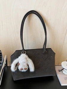Sac fourre-tout en daim marron foncé avec pendentif lapin gris sur un bureau en bois