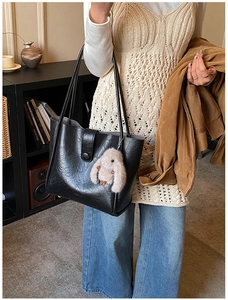 Detail of black pebbled leather tote bag with plush rabbit charm in a cozy lifestyle setting