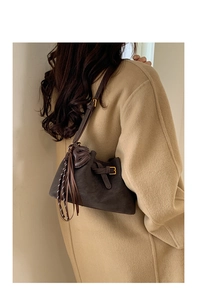 Détail du sac à bandoulière en daim marron avec franges et boucle dorée sur un manteau