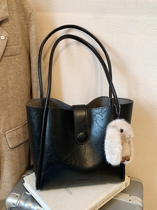 Retro black leather tote bag with plush bunny charm on silver suitcase in warm setting