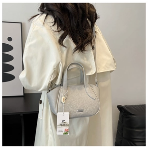 Detailansicht einer hellgrauen Lederhandtasche mit Litschi-Muster und abnehmbarem Gurt