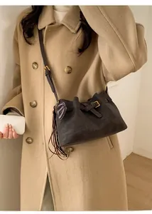 Gros plan d'un sac seau en daim marron foncé avec détails dorés porté par un mannequin