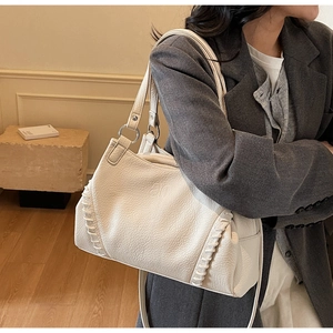 Detailed view of cream leather shoulder bag with decorative cross-stitch and twin handles
