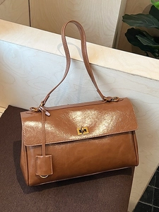 Vintage brown leather crossbody bag with gold buckle on a warm textured background