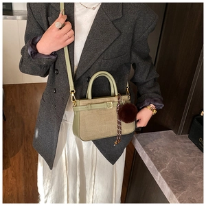 Detail showing woven texture sage green handbag with faux fur pompom on model