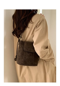 Détail d'un sac seau en daim marron foncé avec rabat porté sur un trench-coat kaki élégant