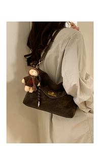 Detail of dark brown faux suede shoulder bag with gold turn-lock and teddy bear charm
