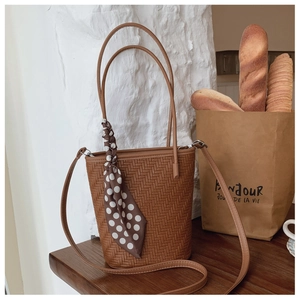 Detail of a brown woven bucket bag with polka dot scarf on a natural wood surface