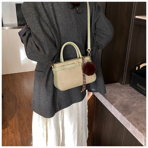 Detail of light green bucket bag featuring woven texture and plush pompom charm