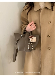 Détail du sac seau gris avec breloque ours en peluche et chaîne perlée sur manteau