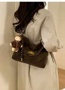 Detail of dark brown hobo bag featuring a gold metal lock and a cute teddy bear pendant