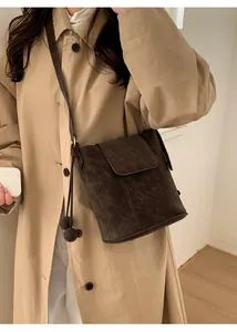 Détail d'un sac cabas en daim marron foncé avec cordons à pompons et rabat de fermeture