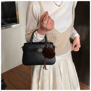 Detail of black woven bucket bag with metal buckle and brown faux fur pompom charm