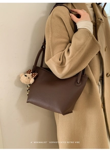 Détail du sac seau en cuir marron foncé avec un porte-clés ours et un nœud élégant