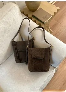 Détail de deux sacs seaux en daim marron foncé avec boucles dorées sur un canapé blanc
