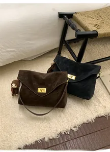 Detail of suede crossbody bags in dark brown and navy with gold square buckles