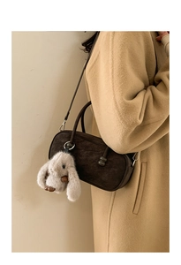 Detail of dark brown suede cylinder bag with a plush bunny charm on a camel coat