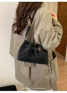 Sac seau minimaliste en daim noir avec boucle dorée vintage porté par un mannequin