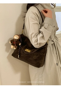 Detail of dark brown faux suede shoulder bag with gold metal lock and teddy bear charm