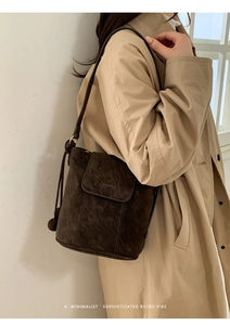 Détail du sac seau en daim marron mat avec bandoulière porté par un mannequin chic