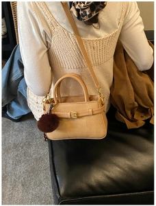 Close-up of woven camel bucket bag featuring gold hardware and a fluffy brown pompom charm