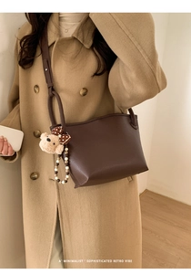 Détail du sac seau en cuir marron foncé avec breloque d'ours porté à l'épaule