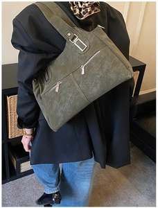 Detailed view of an olive green tote bag with multiple zip pockets on a casual outfit
