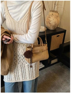 Detail showing khaki woven bucket bag with brown pompom and adjustable strap on a model
