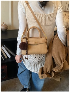 Close-up of khaki woven bucket bag with leather handle and plush ball charm accessory