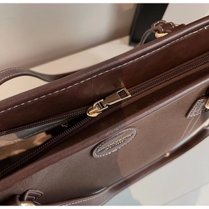 Detail of dark brown leather tote bag showing gold zipper and textured interior lining