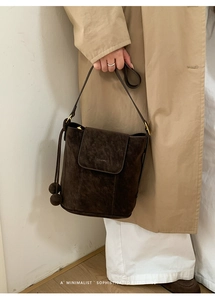Détail du sac seau en cuir mat marron foncé avec pompon latéral et fermoir magnétique