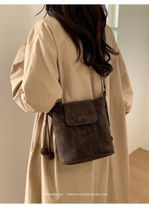 Détail d'un sac seau en daim marron foncé avec breloques sur un trench-coat kaki
