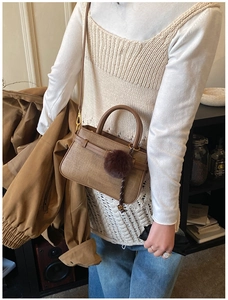 Close-up of brown woven bucket bag with leather strap and plush pom-pom charm detail