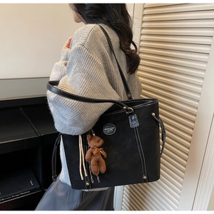 Detail of black tote bag featuring white contrast stitching and cute bear charm pendant