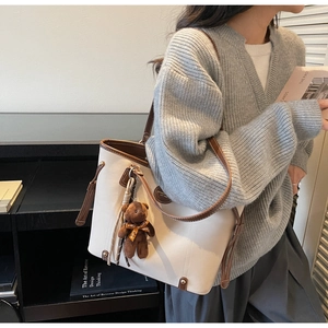 Detail of off-white leather tote bag with brown trim and cute teddy bear charm