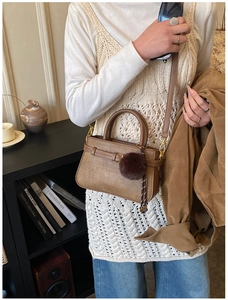 Close-up of brown vintage bucket bag with decorative strap lock and dark plush pompom
