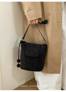 Sac seau noir chic avec détails dorés, porté par un mannequin en trench-coat classique