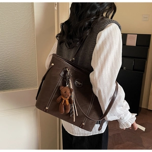 Detail view of large dark brown tote bag with white stitching and bear charm accessory